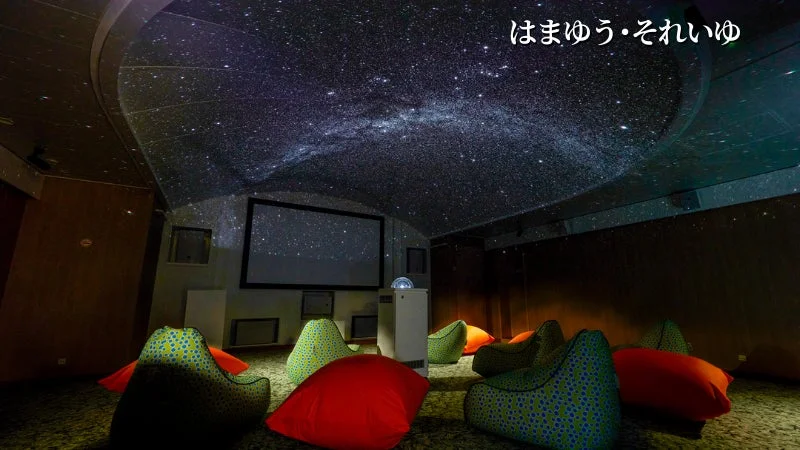 天井に美しい星空が映し出されたドーム型空間で、カラフルなビーズクッションが並べられている