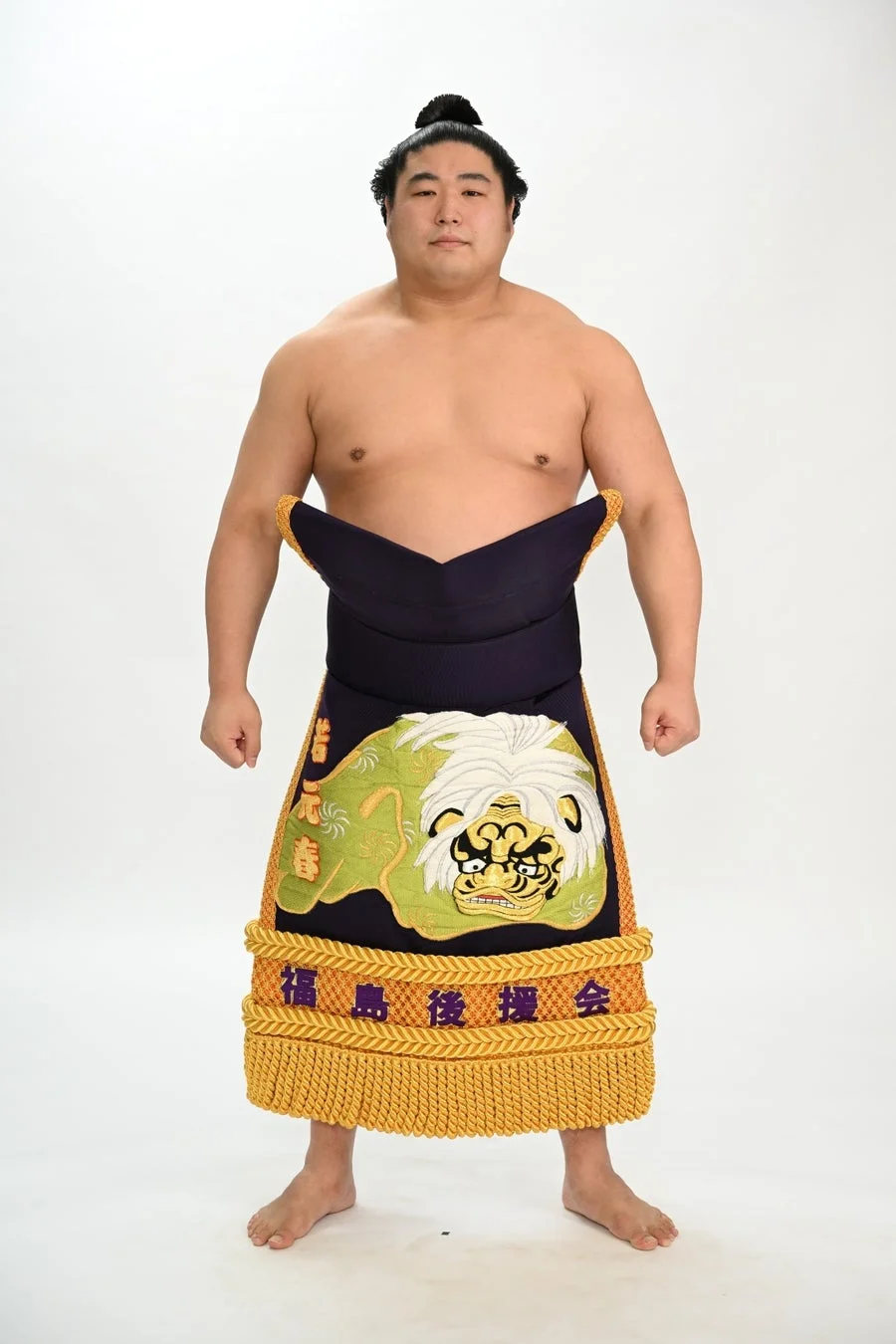 化粧まわしを着用した力士が正面を向いて立っています。化粧まわしには「諸元春」の文字と獅子の刺繍、「福島後援会」の文字が見られます。