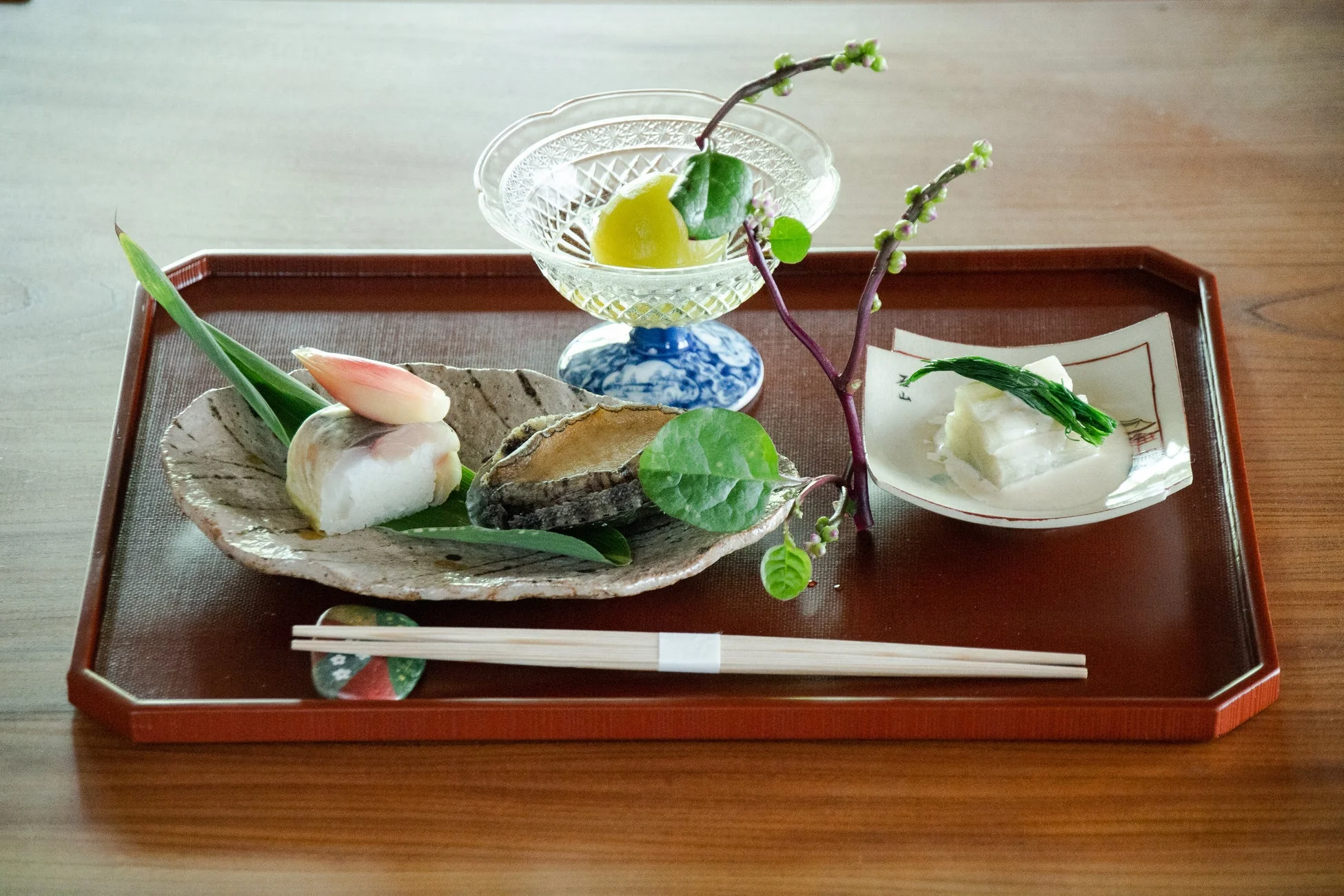 木製の膳に美しく盛り付けられた伝統的な和食の料理が並んでいます。魚料理、鮑、酢の物、柑橘系のデザートなど、彩り豊かで繊細な品々が上品な食事のシーンを演出しています。