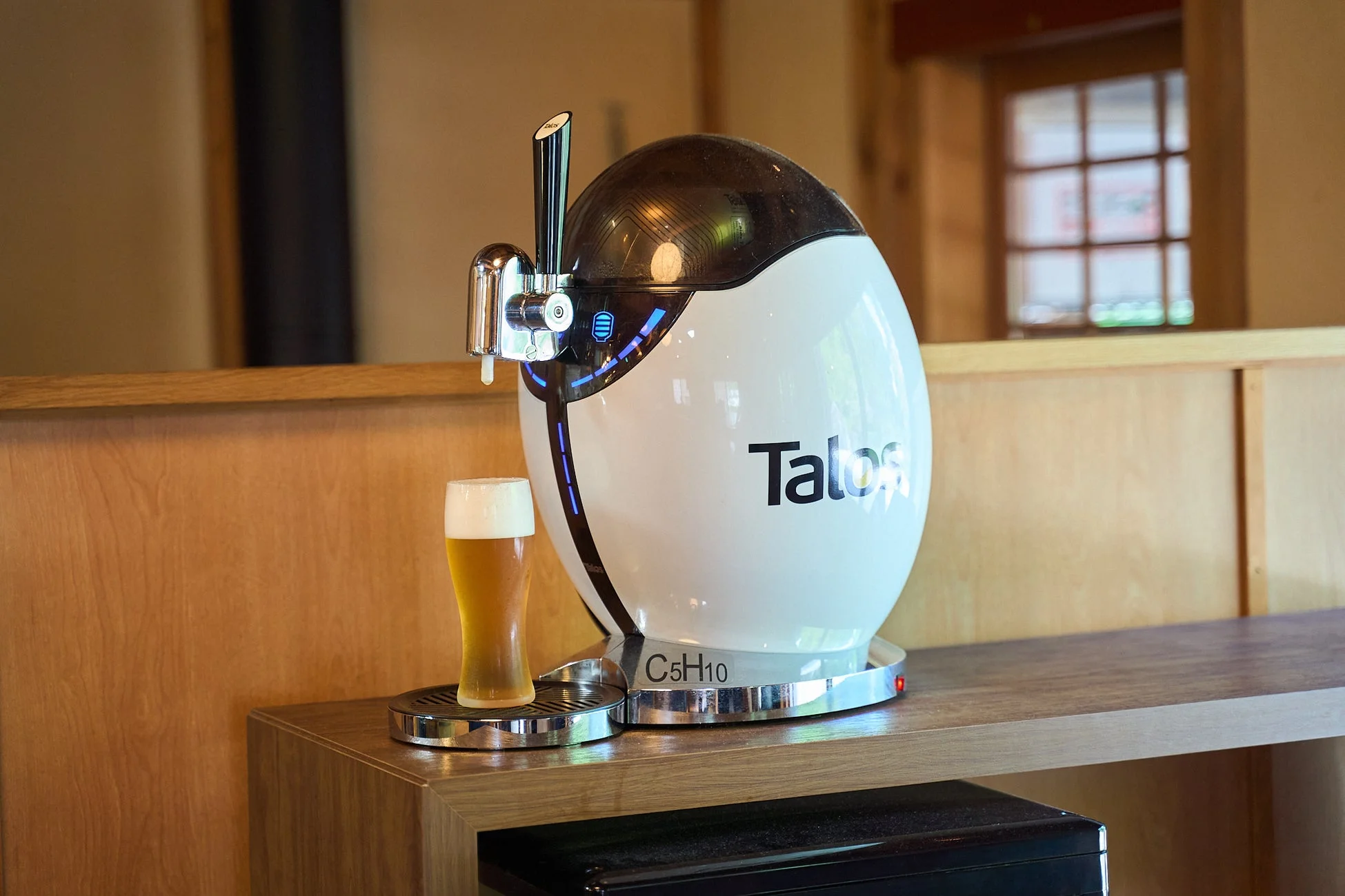 モダンなデザインのビールサーバーが木製のカウンターに置かれ、注がれたビールグラスが隣にあります。温かみのある屋内の雰囲気です。